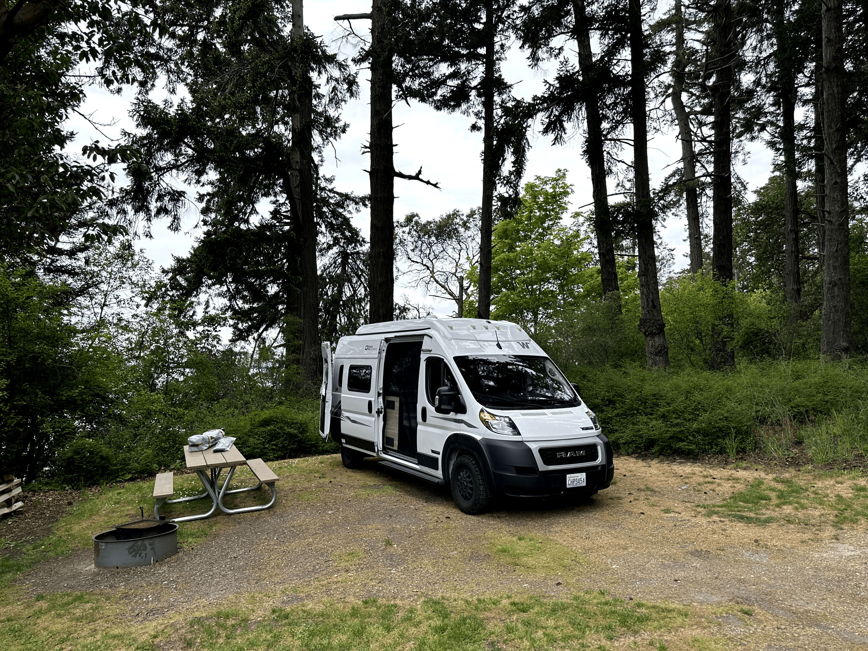 Tranquil campervan parked in forest with picnic table and fire pit.