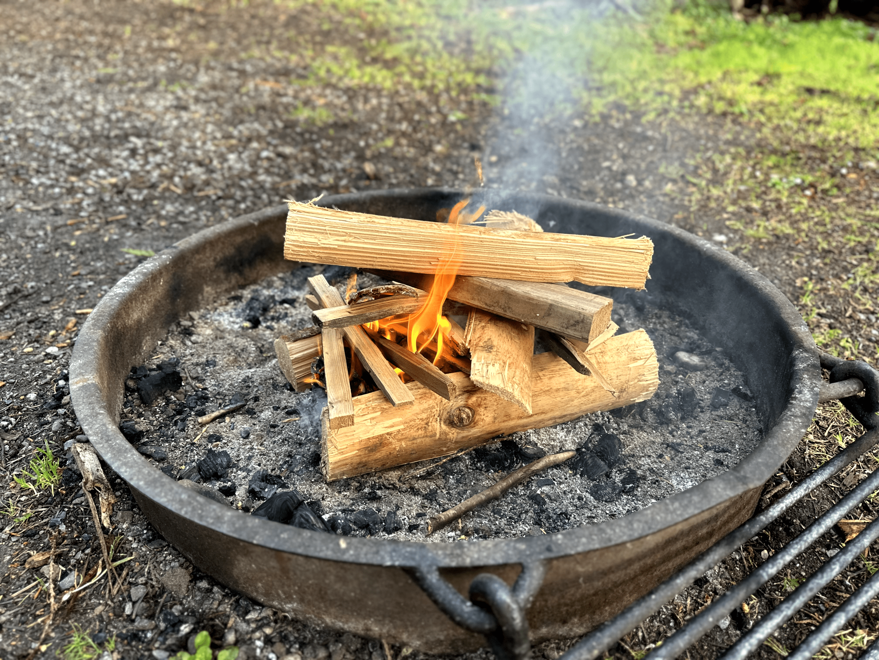 Neatly arranged campfire burning in metal fire pit on outdoor camping site.