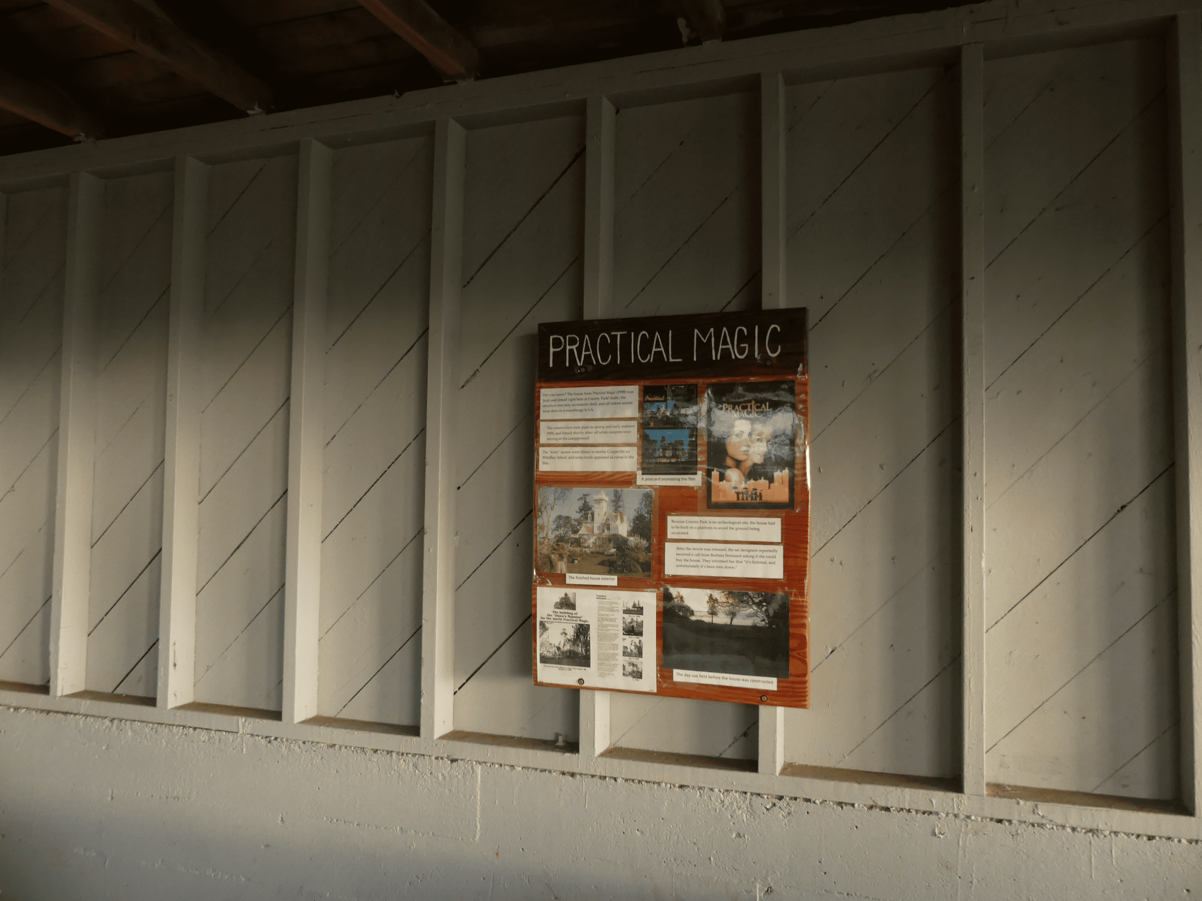 Rustic wall-mounted informational display featuring Practical Magic poster in aged interior setting.
