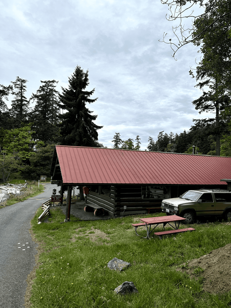 Rustic log cabin with red roof, porch, and car in grassy setting.