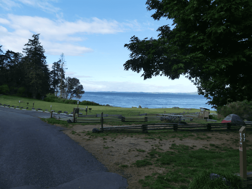 Tranquil park setting overlooking water with picnic benches, grassy area, and blue sky.