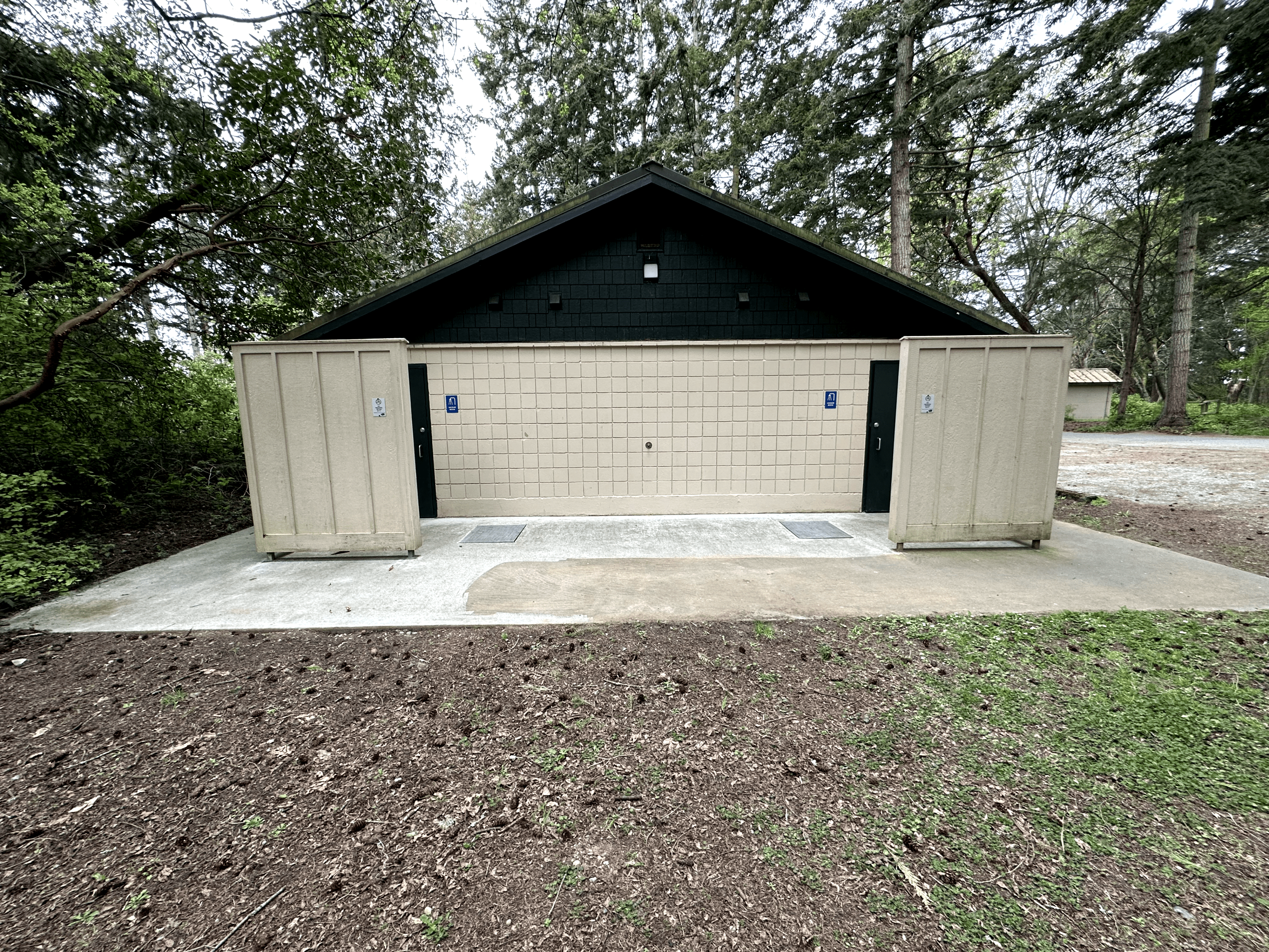 Public restroom facility in serene park setting with green doors and wheelchair accessibility signs.